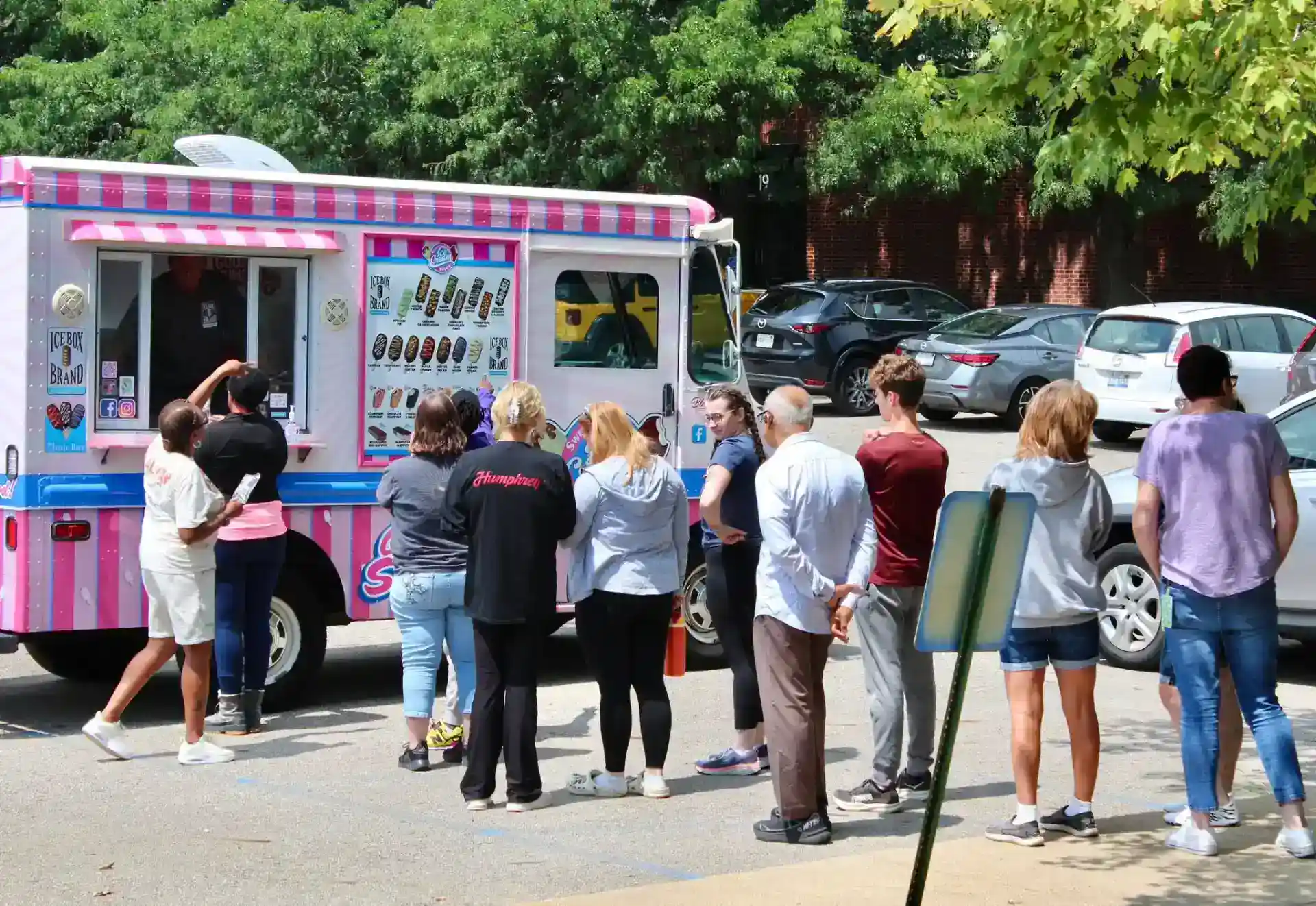 People ordering ice cream from a pink and white ice cream truck.