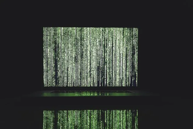Matrix code on a computer screen with green digital rain effect, representing cybersecurity or coding concepts, dark background with reflection below, digital data, programming, and cyber security imagery.