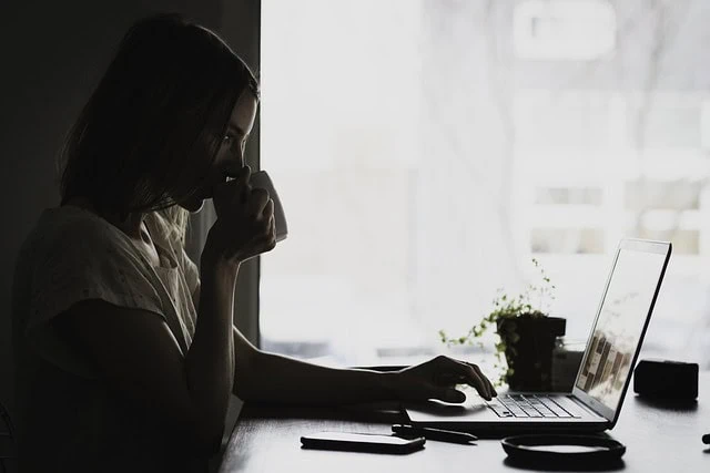 Calm woman drinking tea while working on a laptop at home, soft natural light, modern workspace, peaceful and productive atmosphere, Link Tea branding.