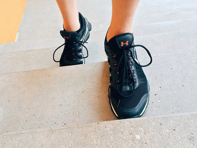 Running shoes by Under Armour on concrete staircase, sport footwear for training and running, lightweight athletic sneakers, black with red accents, designed for performance and comfort in exercise routines.