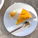 A slice of passion fruit tart, its glaze dotted with glossy black seeds, served with a physalis