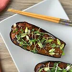 Aubergine au miso laquée, parsemée de ciboule, de jeunes pousses et de sésame, avec des baguettes