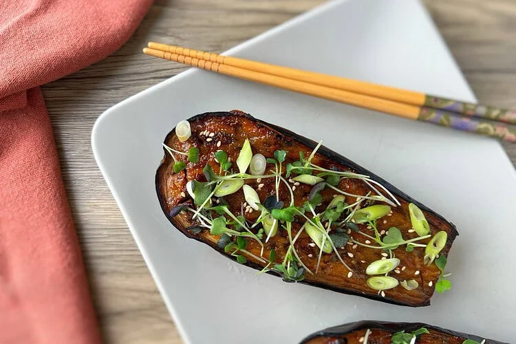 Aubergine au miso laquée, parsemée de ciboule, de jeunes pousses et de sésame, avec des baguettes