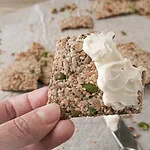 Hand holding a homemade seed cracker topped with fresh goat cheese