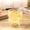 Ginger lemon honey tea in a double-walled glass, with a lemon slice and a spoon, on a light wood countertop