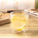 Ginger lemon honey tea in a double-walled glass, with a lemon slice and a spoon, on a light wood countertop