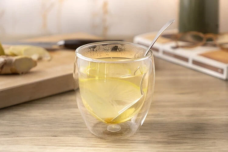 Infusion gingembre citron dans un verre à double paroi, avec une rondelle de citron et une cuillère