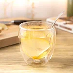Infusion gingembre citron dans un verre à double paroi, avec une rondelle de citron et une cuillère, sur un plan de travail en bois clair