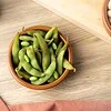Bol en terre cuite rempli d’edamame cuits dans leur gousse, sur une table en bois clair