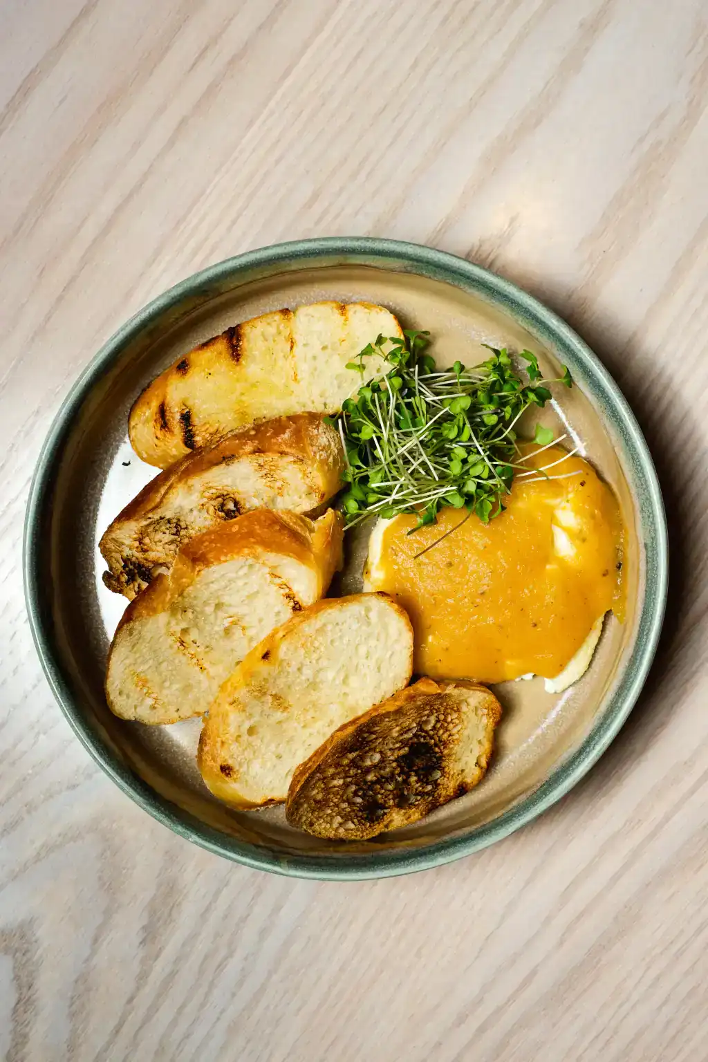 Baked goat cheese served with toasted bread and fresh greens on a ceramic plate.