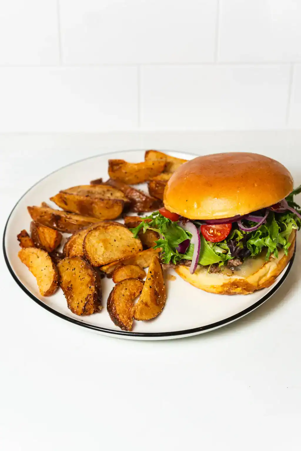 Delicious house burger with fresh vegetables and crispy potato wedges on a white plate.