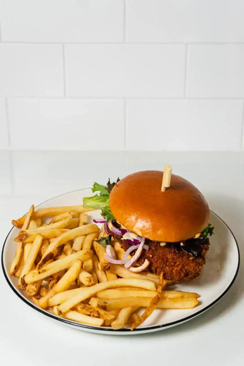 Crispy chicken sandwich with lettuce, onions, and fries on a white plate.