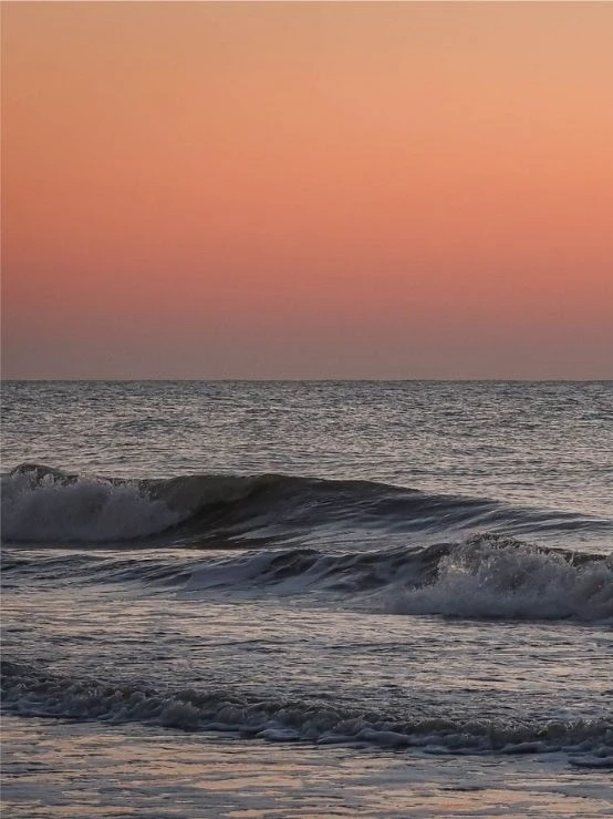 Gentle ocean waves at sunset under a soft pink sky, capturing a calm coastal scene in St. Simons Island Georgia, evoking the perfect scene for pairing with vitamin sea quotes.