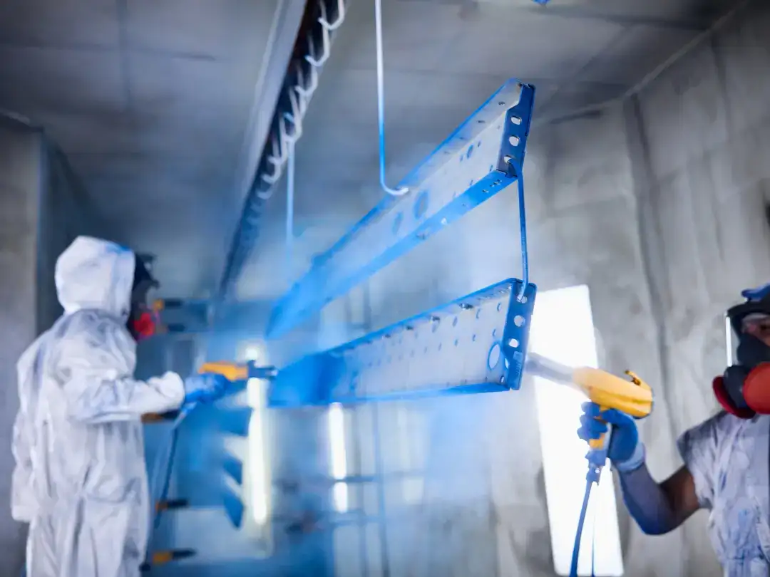 Workers welding metal parts in a factory setting with safety gear.