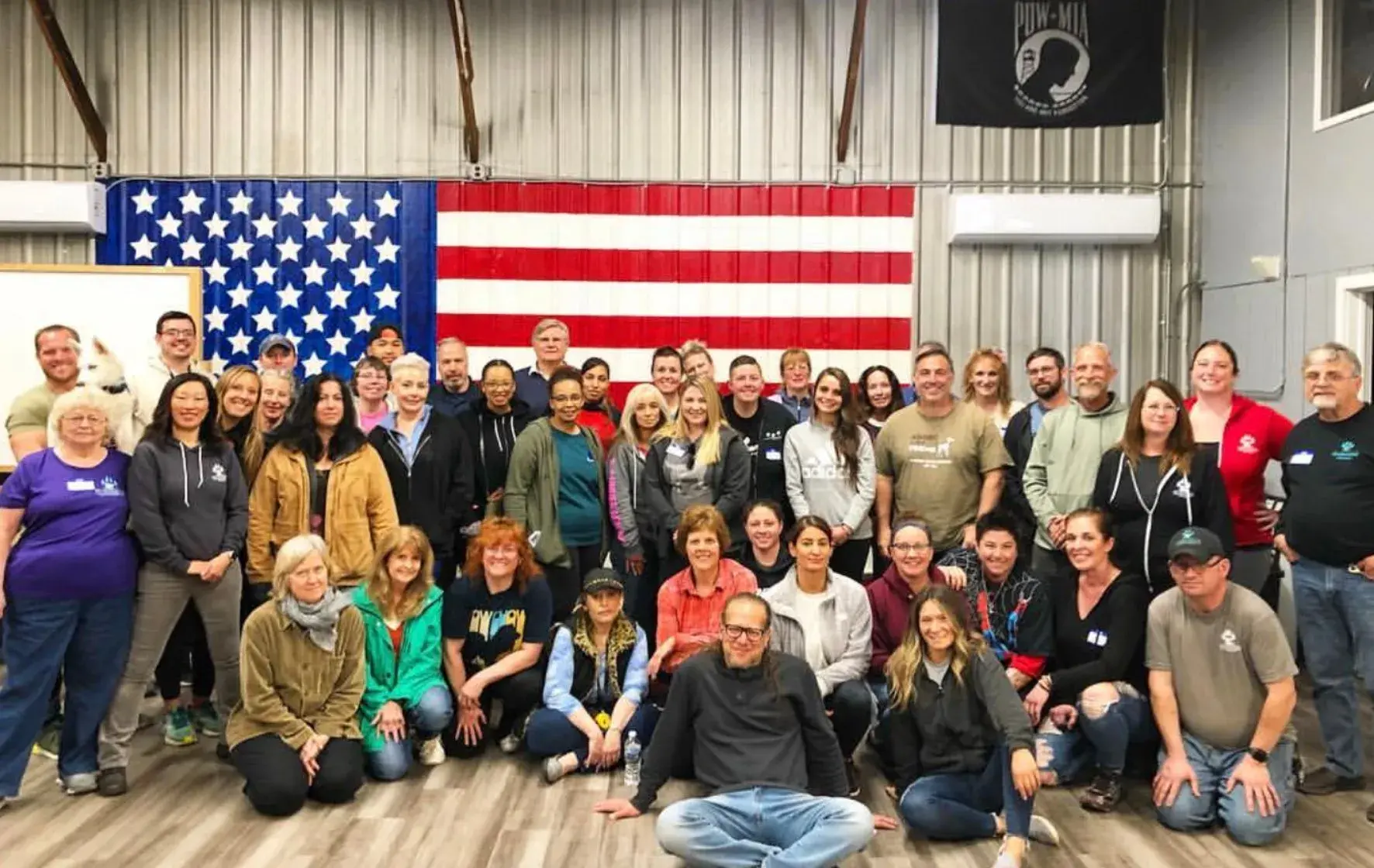 Group of people posing for a photo in a room with an American flag in the background after a dog training session.