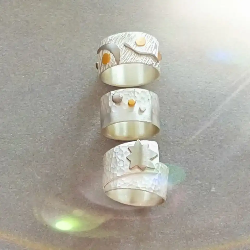 Drei Silberringe mit verschiedenen Designs, darunter Stern- und Mondmuster sowie eine strukturierte Oberfläche.
