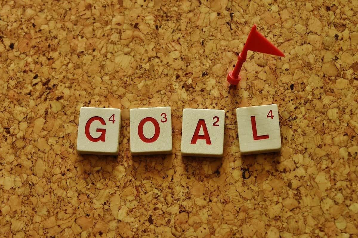 The word goal spelled out on a corkboard using Scrabble tiles.