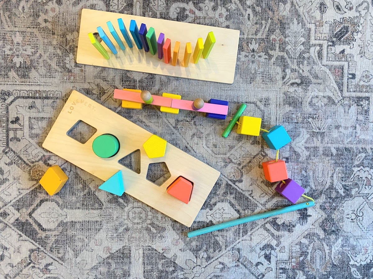 Pieces from the Lovevery wood block set set up to show it can be used as a shape sorter, as dominos, as a threading toy, and as a building toy, among other ways to play