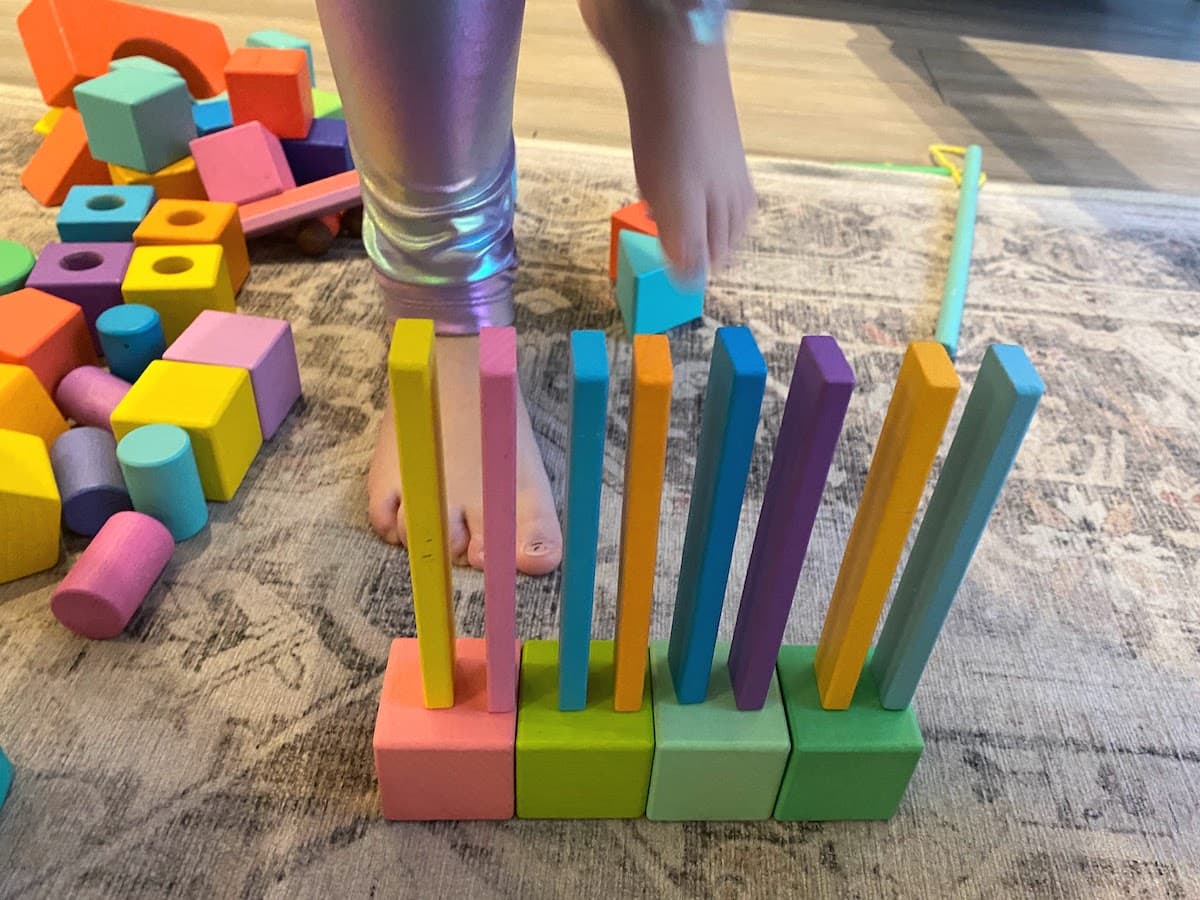 Lovevery wooden blocks built using blocks and wooden planks. A child's legs and feet are visible.