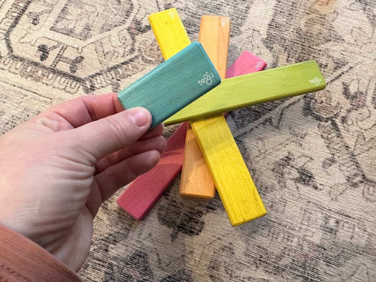 A woman's hand holds a Tegu wooden block, showing that the magnets are not visible in this magnetic wooden block set