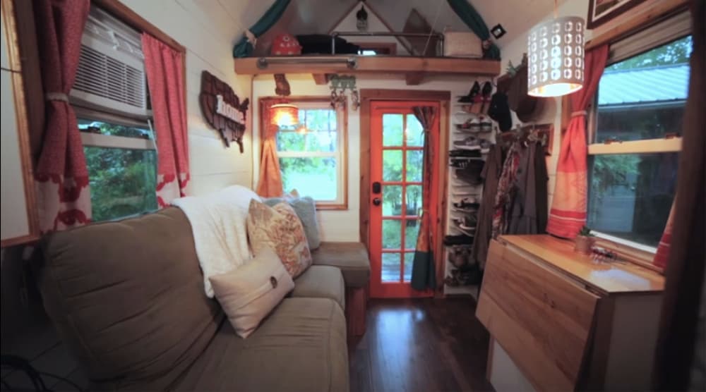 Tiny home living area with a tiny house couch, space saving shoe storage and fold down table.