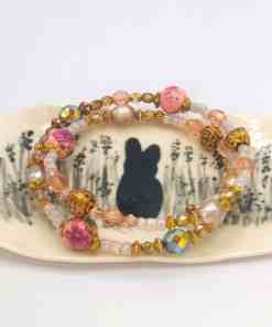 Two beaded bracelets with gold, pink, and pearl elements placed on a Bunny Jewellery Holder featuring a silhouette of a rabbit surrounded by plants.