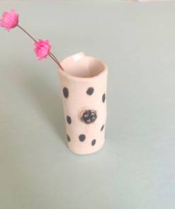 Speckled Mini Pottery Vase, featuring a black polka dot design, holding two small pink flowers, set against a light green background.