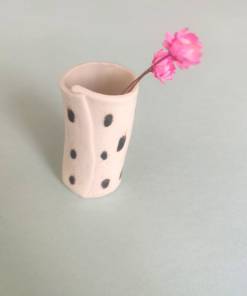 Speckled Mini Pottery Vase holds a single pink flower against a pale blue background.