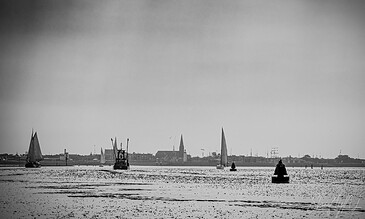 Sailboats on calm water with a distant cityscape and church spires, captured in black and white, showcasing peaceful maritime scenery and serene moments.