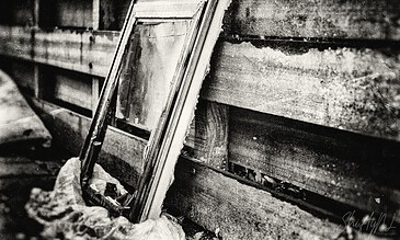An old broken mirror leaning against a weathered wooden wall, capturing a moment of decay and nostalgia in black and white.