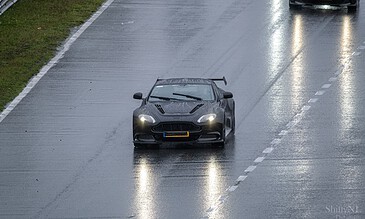 1. Black sports car driving on a rainy wet road, high-performance vehicle, sleek design, in motion during rainy weather, automotive photography.