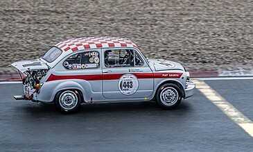 1. Vintage Fiat Abarth race car speeding on track with racing decals and red-and-white checkered roof, showcasing classic motorsport excitement.