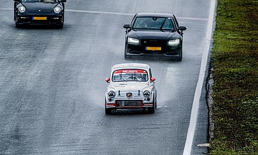 Classic race cars navigating wet track during a vintage motorsport event.