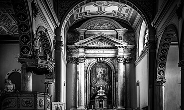 Intricate black and white photo of a historic church interior with classical architecture, ornate columns, and religious artwork behind the altar.
