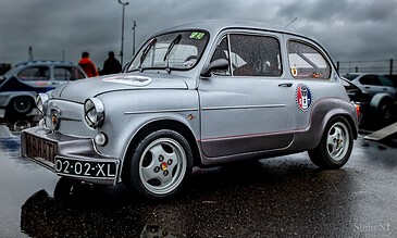 1. Vintage gray Fiat 500 displayed outdoors on a rainy day, with water droplets on the car and a cloudy sky in the background.