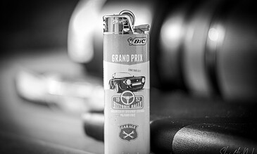 A vintage BIC lighter with a "Grand Prix" racing theme, featuring a classic car illustration, placed on a wooden surface with blurred automotive parts in the background.