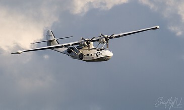 A vintage military aircraft in flight, showcasing its propellers and sleek design against a backdrop of clouds. Aero Commander military aircraft flying through cloudy sky during daytime.