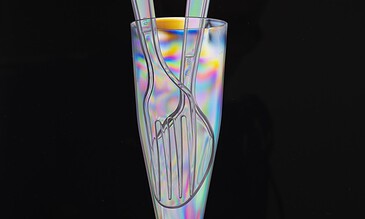 Vibrant iridescent glass vase containing silver fork and spoon against a black background, artistic still life. Colorful iridescent glass with silver utensils inside, artistic still life photography.