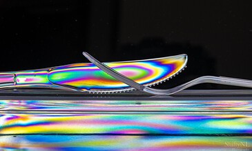 Vivid rainbow-colored iridescent spoon and fork captured in close-up, showcasing the shimmering metallic effect and reflective surface in a modern still life composition. Colorful iridescent spoon and fork set on reflective surface with a black background, highlighting vibrant rainbow hues and intricate details for artistic food photography.