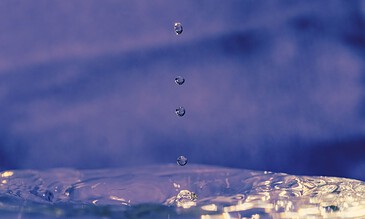 Water droplets falling into a blue liquid, creating ripples and reflections. Capturing the mesmerizing movement and clarity of water droplets in a close-up shot.