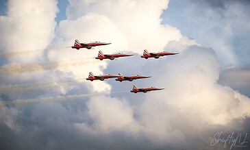 Spectacular aerial display featuring five red jets soaring in a tight formation against a backdrop of dramatic clouds. Red jet aircrafts flying in formation through a cloudy sky during an airshow.