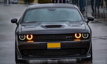 1. Front view of a black Dodge Challenger SRT with illuminated headlights on a rainy street.