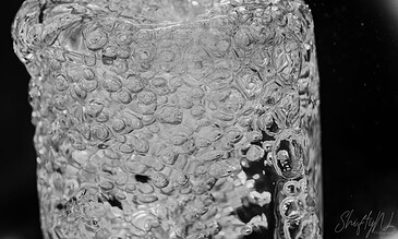 1. Close-up of bubbling ice cube in water, black background, high detail, monochrome, emphasizing texture and clarity.