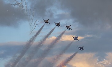 Spectacular display of five fighter jets performing a synchronized aerial maneuver with vibrant smoke trails at an airshow. Aero military jets flying in formation during an airshow, leaving colorful smoke trails against a partly cloudy sky.