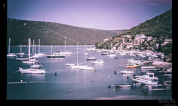 Colorful marina with boats docked in a tranquil harbor surrounded by lush green hills during daytime.
