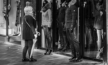 2. A shopper with an umbrella interacts with mannequins wearing stylish winter apparel outside a fashion boutique. 1. Mannequins dressed in winter jackets and leather pants displayed in a clothing store window on a city street.