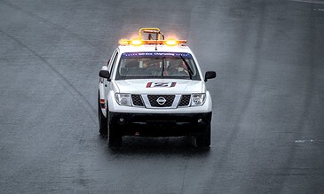 A safety car with flashing lights driving on a wet road during rainy weather, capturing intense moments of emergency response.