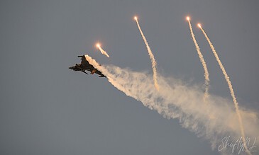 Spectacular military aircraft display with flares and smoke trails, showcasing precision flying and aerial maneuvers. Aero fighter jet launching flares with bright trails against a cloudy sky during an airshow.