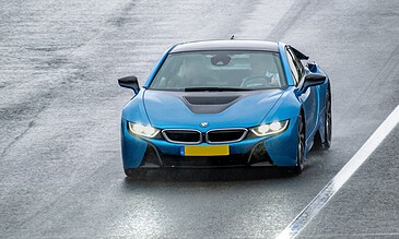 A sleek blue BMW i8 sports car driving on a wet road during rainfall, showcasing modern design and high performance in a dynamic motion.