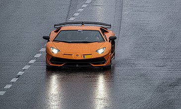Vivid orange Lamborghini Huracán driving on a wet road, showcasing luxury sports car photography in rainy conditions for a stunning visual impact.